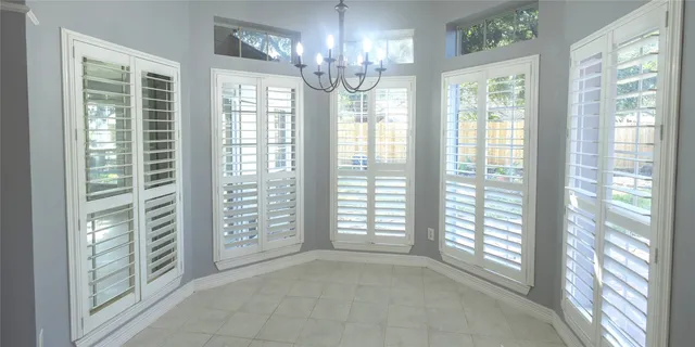 an empty room with wooden floor chandelier fan and windows