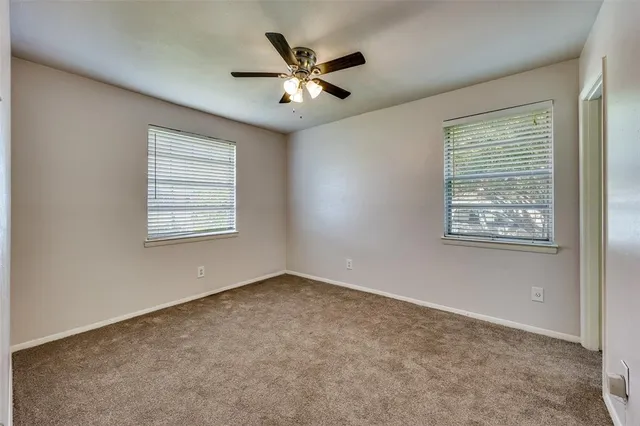 an empty room with ceiling fan and windows