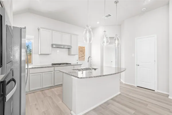 a large kitchen with stainless steel appliances kitchen island granite countertop a refrigerator a stove a sink and white cabinets with wooden floor