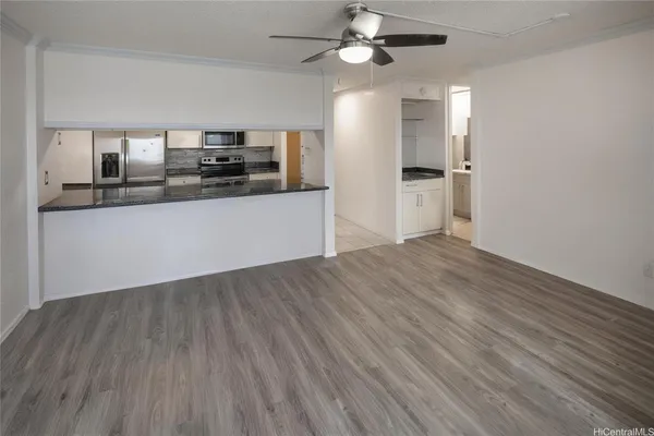 an empty room with wooden floor kitchen view and a window