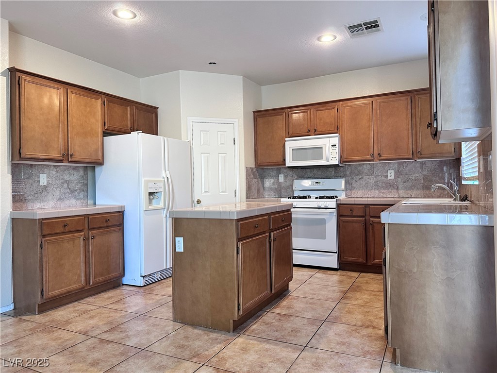 9676 Ridgebluff Avenue Las Vegas, NV 89148 - Photo 6 of 15 Kitchen featuring a kitchen island, white appliances, decorative backsplash, light tile patterned floors, and recessed lighting