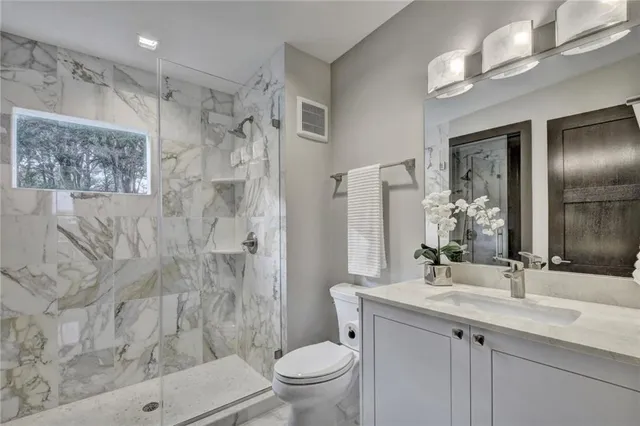 a bathroom with a granite countertop sink a toilet a shower and a mirror
