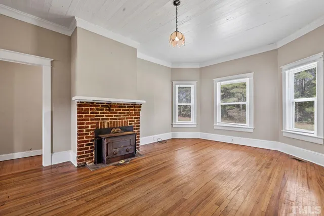 a view of an empty room with wooden floor fireplace and a window