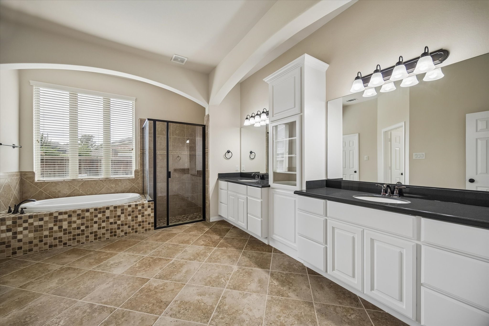 17403 Astrachan Road Richmond, TX 77407 - Photo 17 of 40 This spacious bathroom features a large soaking tub, a glass-enclosed shower, dual sinks with ample counter space, and elegant tile flooring. Natural light pours in through a sizable window, enhancing the room's airy feel.
