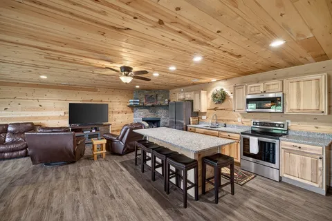a open kitchen with stainless steel appliances granite countertop a stove top oven a sink dishwasher a dining table and chairs with wooden floor