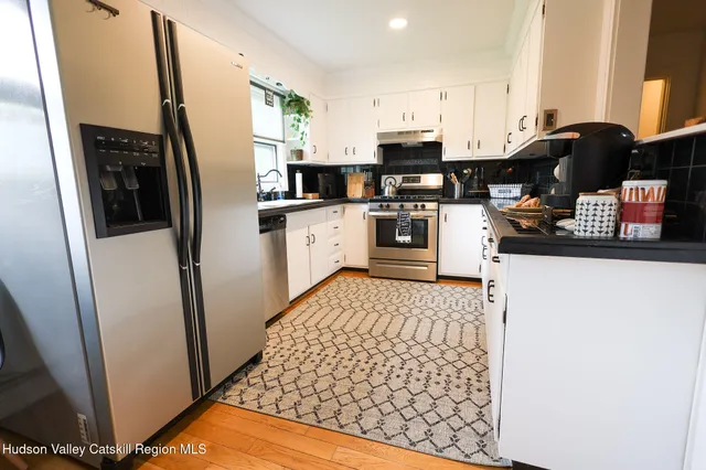 a kitchen with stainless steel appliances a sink a stove a refrigerator a dining table and chairs with wooden floor