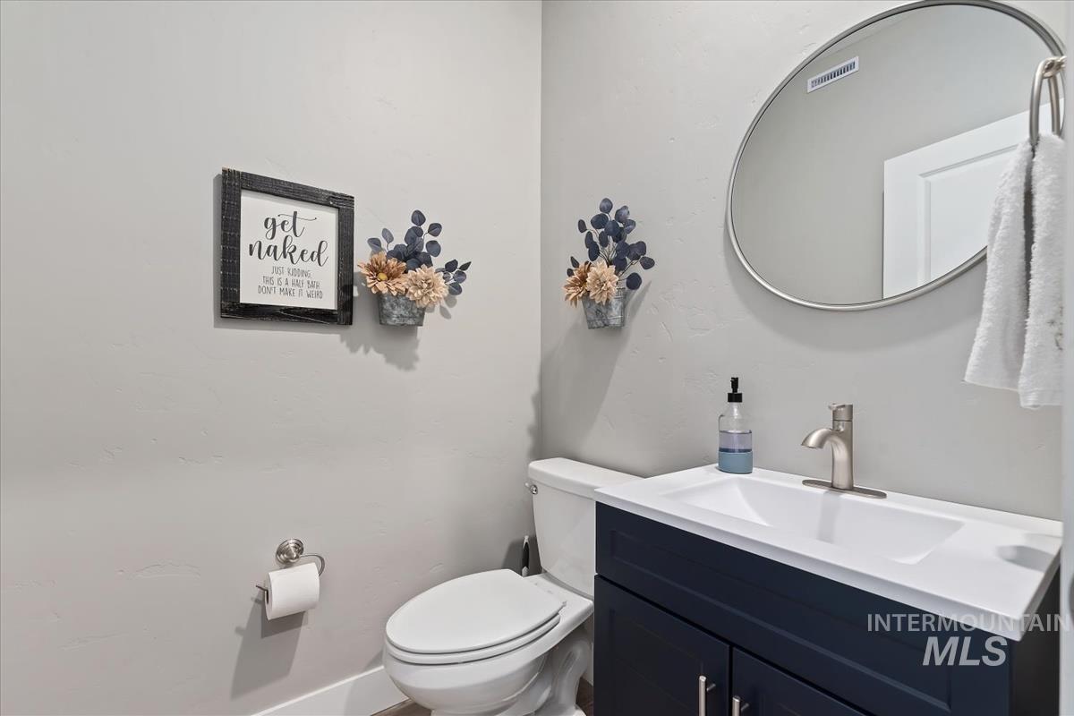 815 Knowledge Street Middleton, ID 83644 - Photo 21 of 49 Modern powder room featuring a white single-basin vanity with a dark blue cabinet base, brushed nickel faucet, and a circular wall-mounted mirror