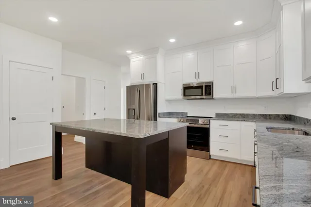 a kitchen with stainless steel appliances granite countertop a stove a refrigerator a sink a microwave and white cabinets with wooden floor