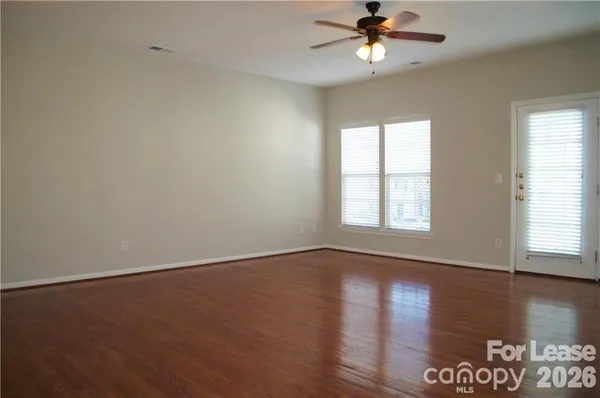 an empty room with wooden floor chandelier fan and windows