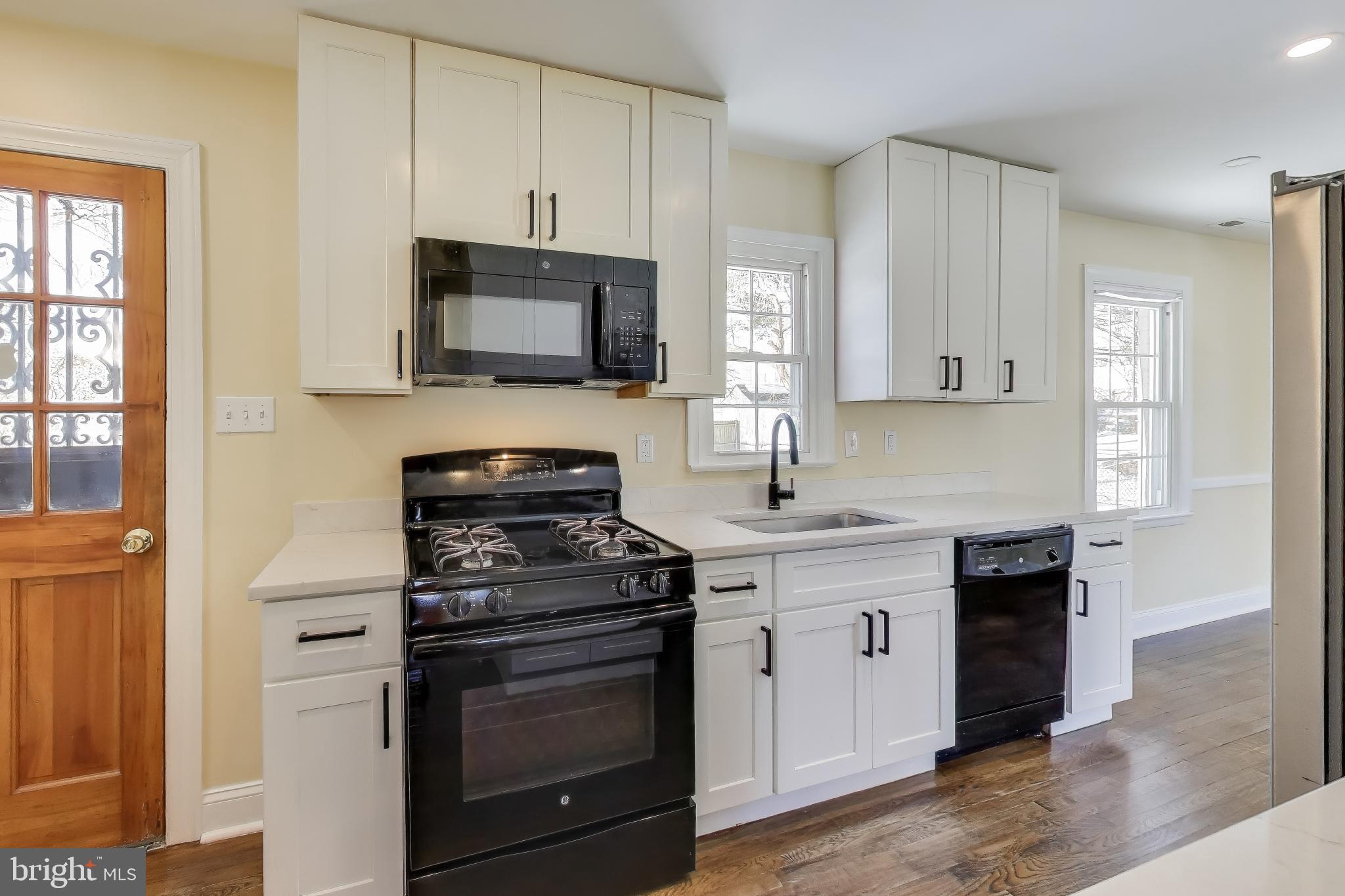6904 Riggs Road Hyattsville, MD 20783 - Photo 3 of 34 a kitchen with stainless steel appliances granite countertop white cabinets a sink a stove a microwave and wooden floors