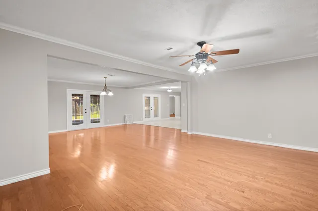 a view of an empty room with chandelier fan and wooden floor