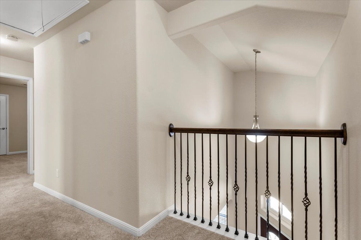3451 Mayfield Ranch Boulevard, Unit 311 Round Rock, TX 78681 - Photo 25 of 40 Second-level landing featuring a wrought iron and wood-finish railing, vaulted ceiling with pendant lighting, and neutral carpet flooring