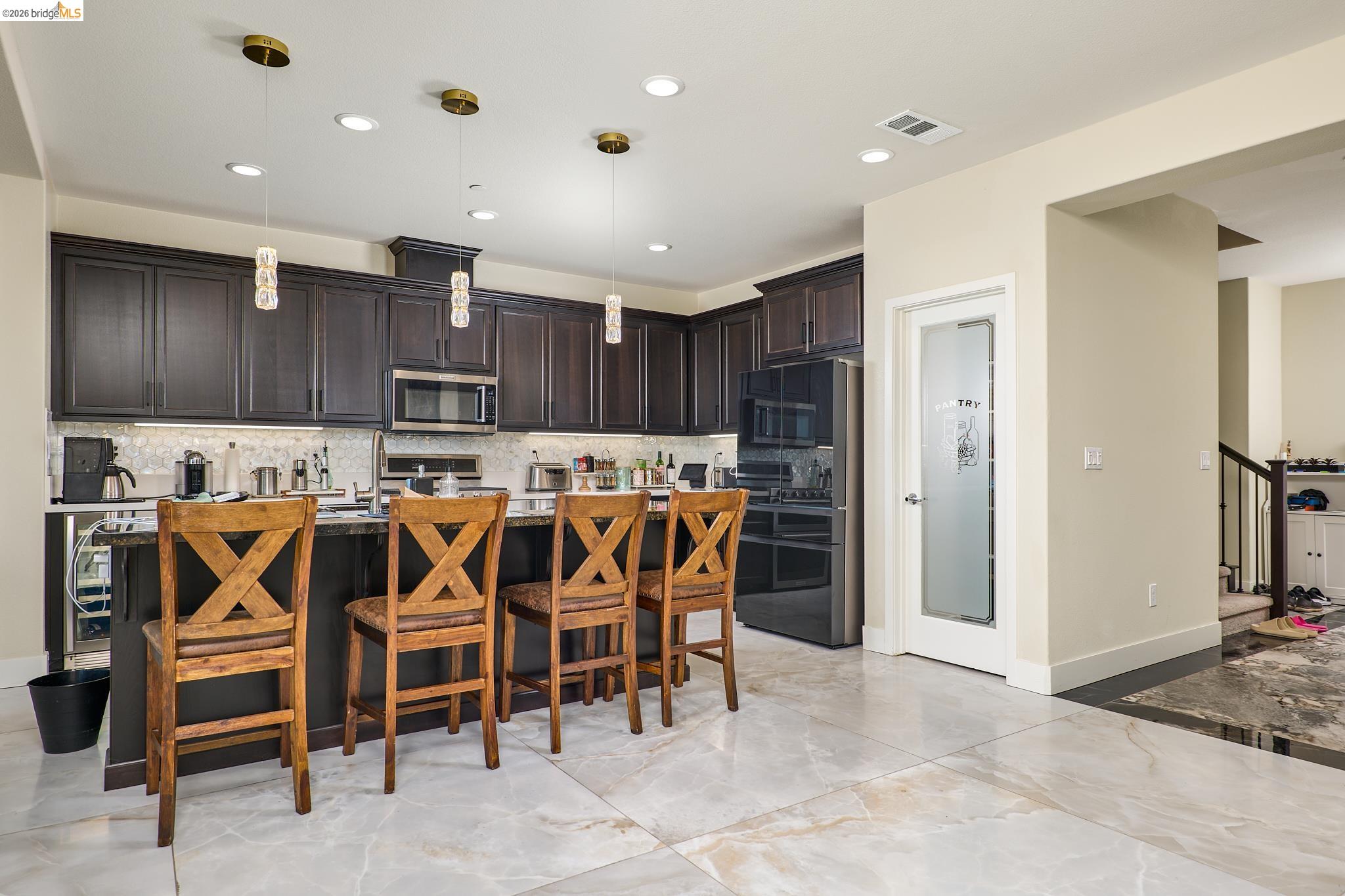 5532 Promontory Way Antioch, CA 94531 - Photo 5 of 45 Kitchen featuring dark wood finish cabinetry, a kitchen island with sink, light stone countertops, light marble finish floors, and stainless steel microwave