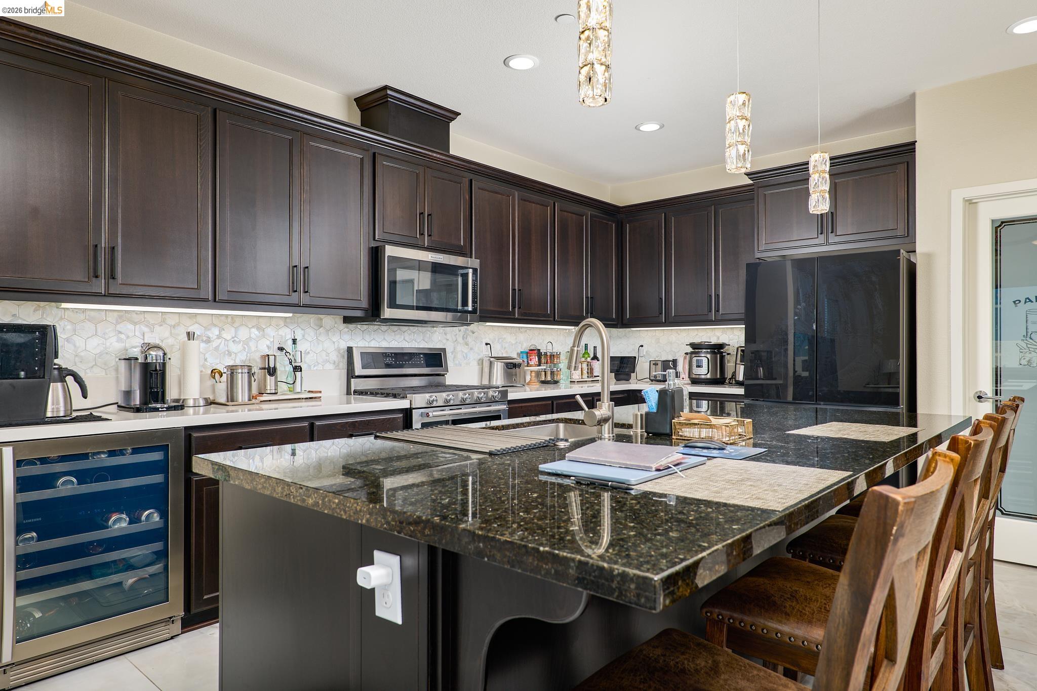 5532 Promontory Way Antioch, CA 94531 - Photo 8 of 45 Kitchen with beverage cooler, dark wood finish cabinetry, stainless steel appliances, dark stone countertops, and a center island with sink