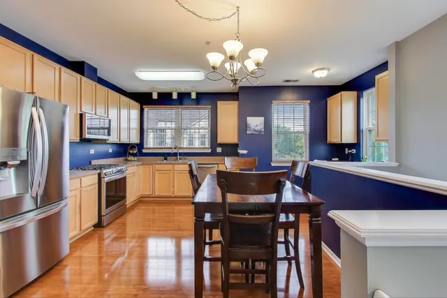a kitchen with stainless steel appliances kitchen island granite countertop a stove a refrigerator a sink dishwasher a dining table and chairs with wooden floor