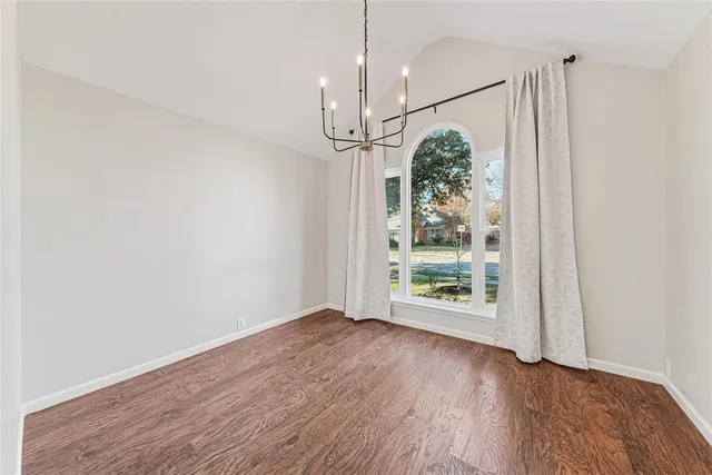 an empty room with wooden floor a chandelier and windows