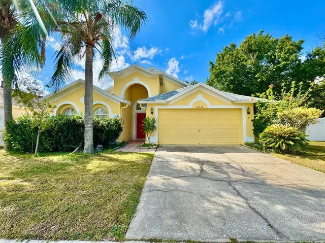 a view of yellow house with a yard and palm trees