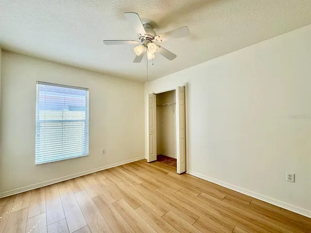 an empty room with wooden floor chandelier fan and windows