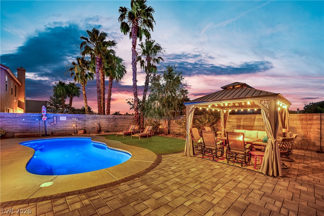 1724 Millstream Way Henderson, NV 89074 - Photo 47 of 60 A tranquil evening setting with a luminous pool, paved patio, and a welcoming gazebo under a vibrant sky.