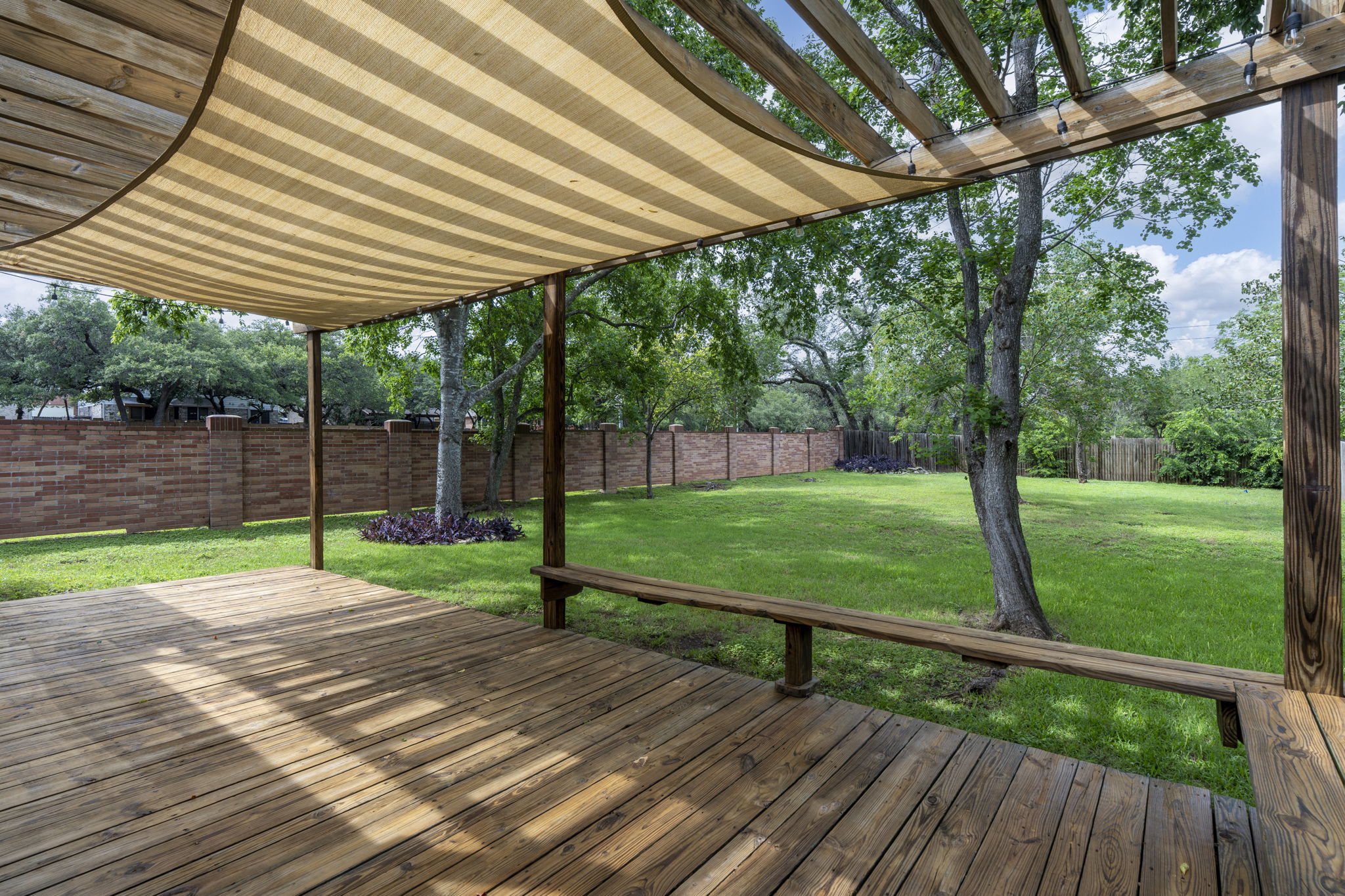 7172 Ridge Oak Road Austin, TX 78749 - Photo 8 of 40 A spacious wooden deck with a shaded pergola overlooks a verdant, fenced yard.