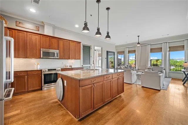 a large kitchen with stainless steel appliances granite countertop a stove a sink dishwasher a microwave oven and a dining table with wooden floor