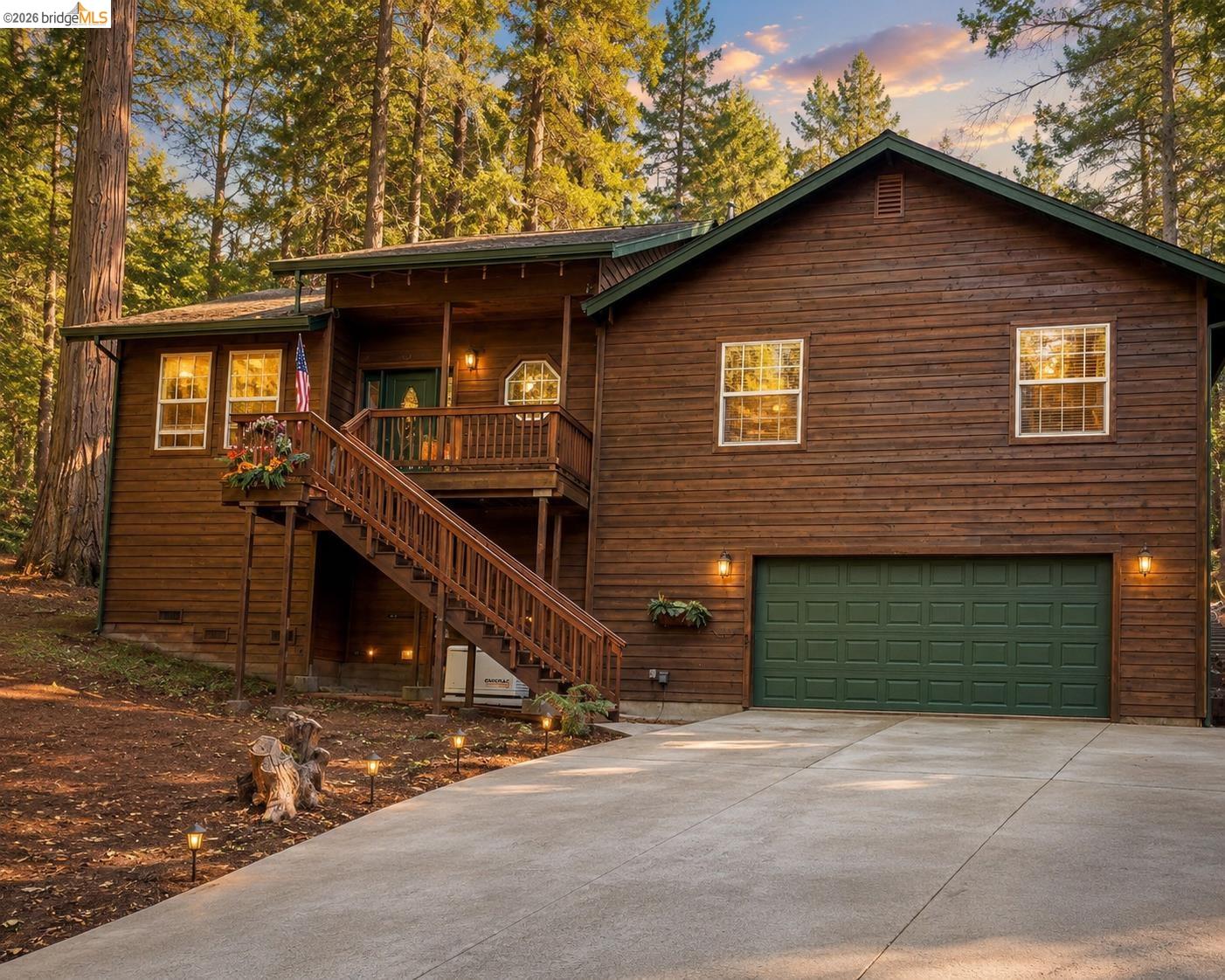 24269 Awahanee Road Sonora, CA 95370 - Photo 1 of 1 Wood-sided exterior featuring an attached two-car garage with a green door, a concrete driveway, and a welcoming front deck with a staircase