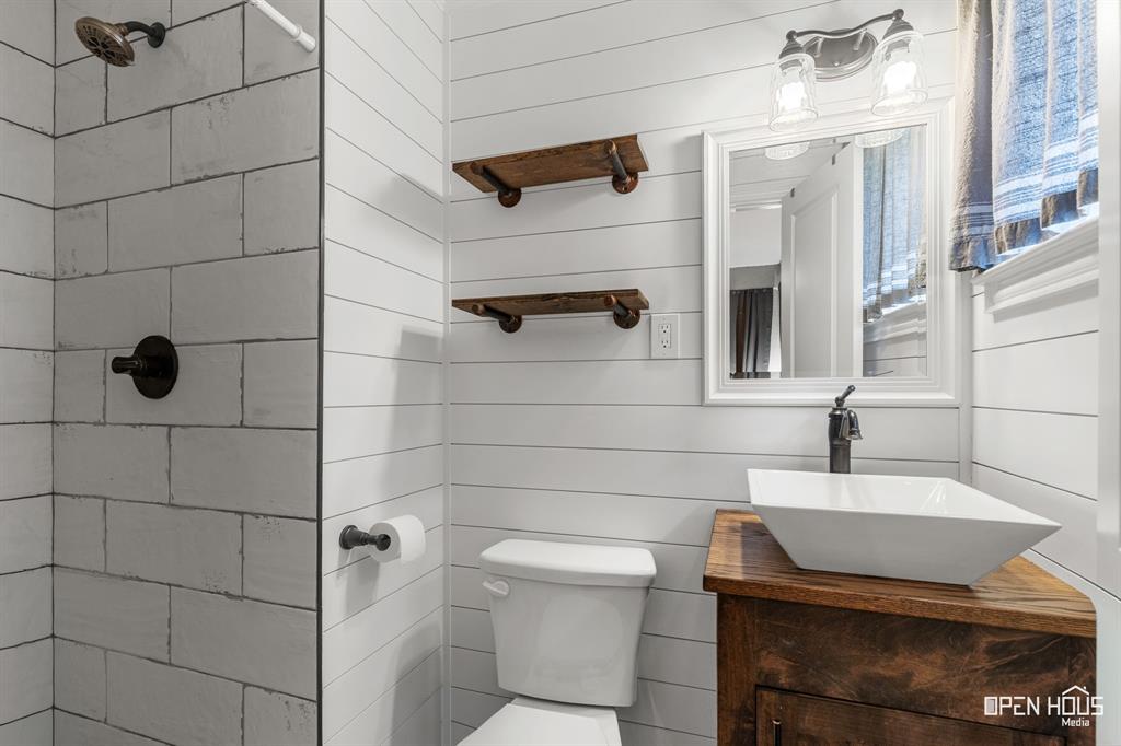 4419 Randel Drive Wichita Falls, TX 76308 - Photo 13 of 32 Shower with subway tile surround and dark bronze fixtures, shiplap wall paneling, wood-finish vanity with vessel sink, and wall-mounted mirror with sconce lighting