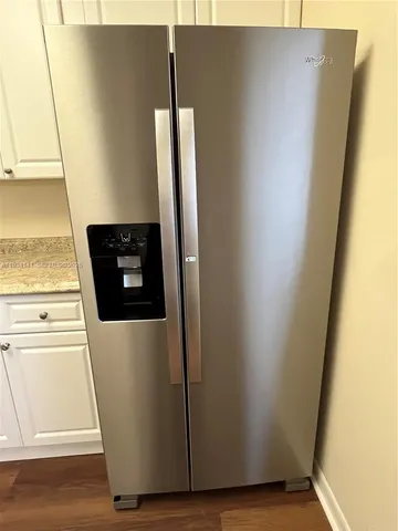a view of a refrigerator in kitchen and an empty room with wooden floor