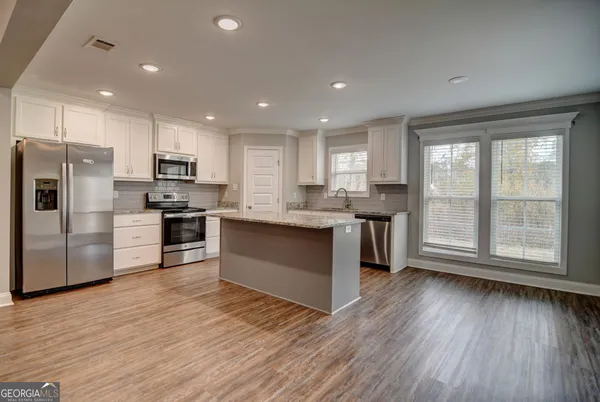 a kitchen with stainless steel appliances granite countertop a refrigerator a sink dishwasher a stove and white cabinets with wooden floor