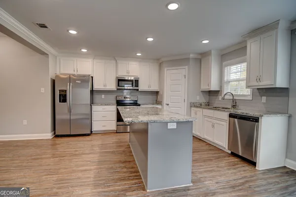 a kitchen with stainless steel appliances granite countertop a refrigerator a stove top oven a sink and dishwasher with wooden floor