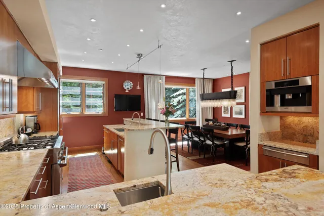 a kitchen with stainless steel appliances kitchen island granite countertop a refrigerator a stove top oven a sink a dining table and chairs