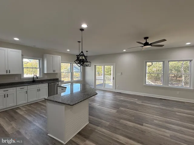 a kitchen with granite countertop a stove a sink and white cabinets with wooden floor