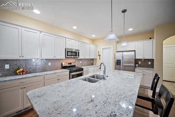 a kitchen with stainless steel appliances kitchen island granite countertop a sink a stove a refrigerator cabinets and chairs