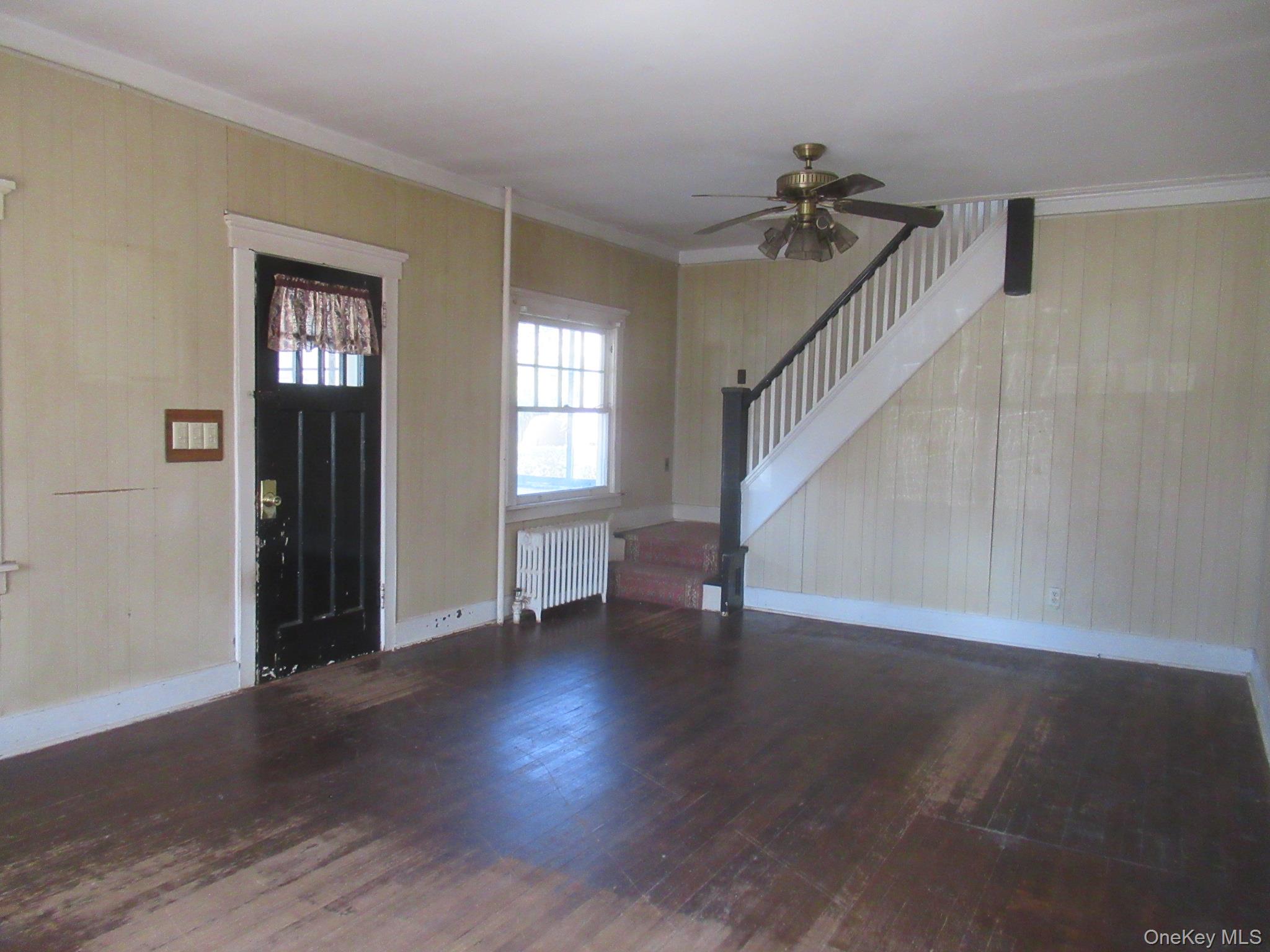 72 Waterstone Road Greenwood Lake, NY 10925 - Photo 10 of 20 Living area featuring wood-finish flooring, a staircase with white balusters and a dark newel post, a ceiling fan, a window with a radiator below, and a multi-pane entry door
