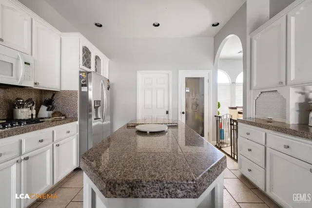 a large kitchen with kitchen island granite countertop a stove a sink a refrigerator and white cabinets