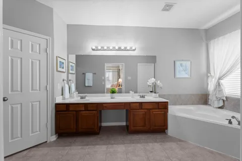 a spacious bathroom with a double vanity sink large mirror bathtub and window