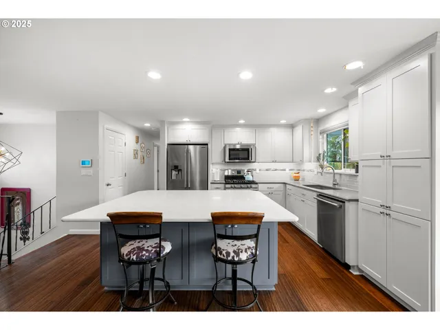 a kitchen with stainless steel appliances kitchen island granite countertop a dining table chairs refrigerator and sink