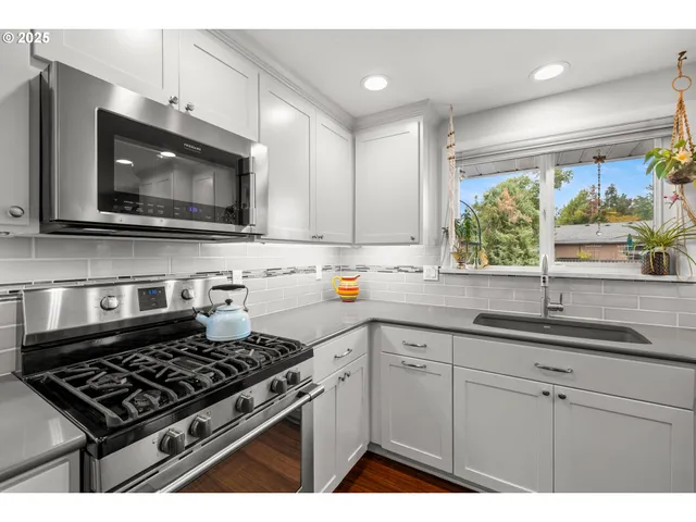 a kitchen with stainless steel appliances a sink a stove a microwave cabinets and a window
