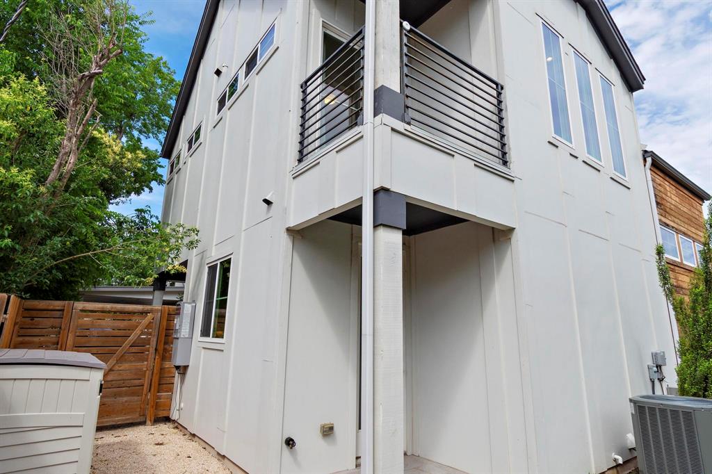 911 Stobaugh Street, Unit 2 Austin, TX 78757 - Photo 24 of 26 Modern exterior featuring light-colored vertical siding, a second-story balcony with horizontal metal railings, multiple large windows, and a private wooden fence