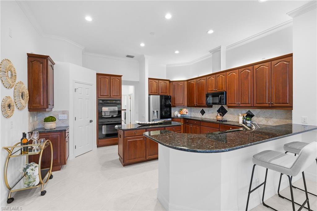 1624 Manchester Court Naples, FL 34109 - Photo 17 of 49 Kitchen with a kitchen island, dark stone counters, crown molding, a breakfast bar area, and black appliances