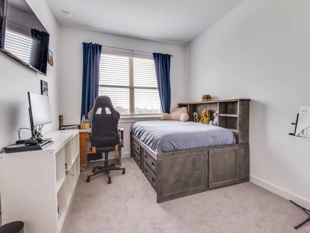a bedroom with a bed a computer on desk and a dresser next to a window