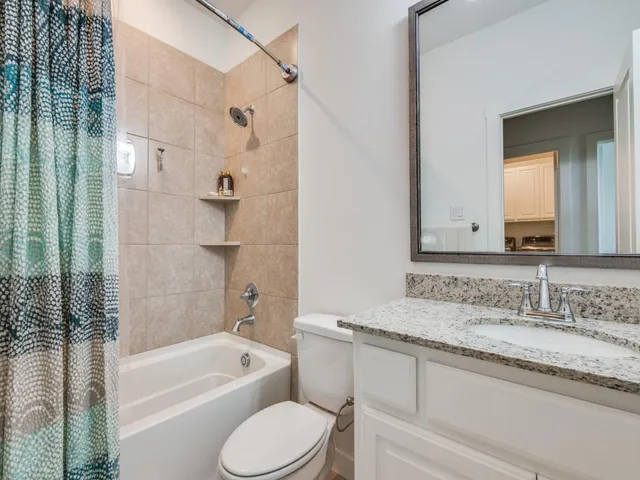 a bathroom with a granite countertop bathtub shower sink vanity and toilet