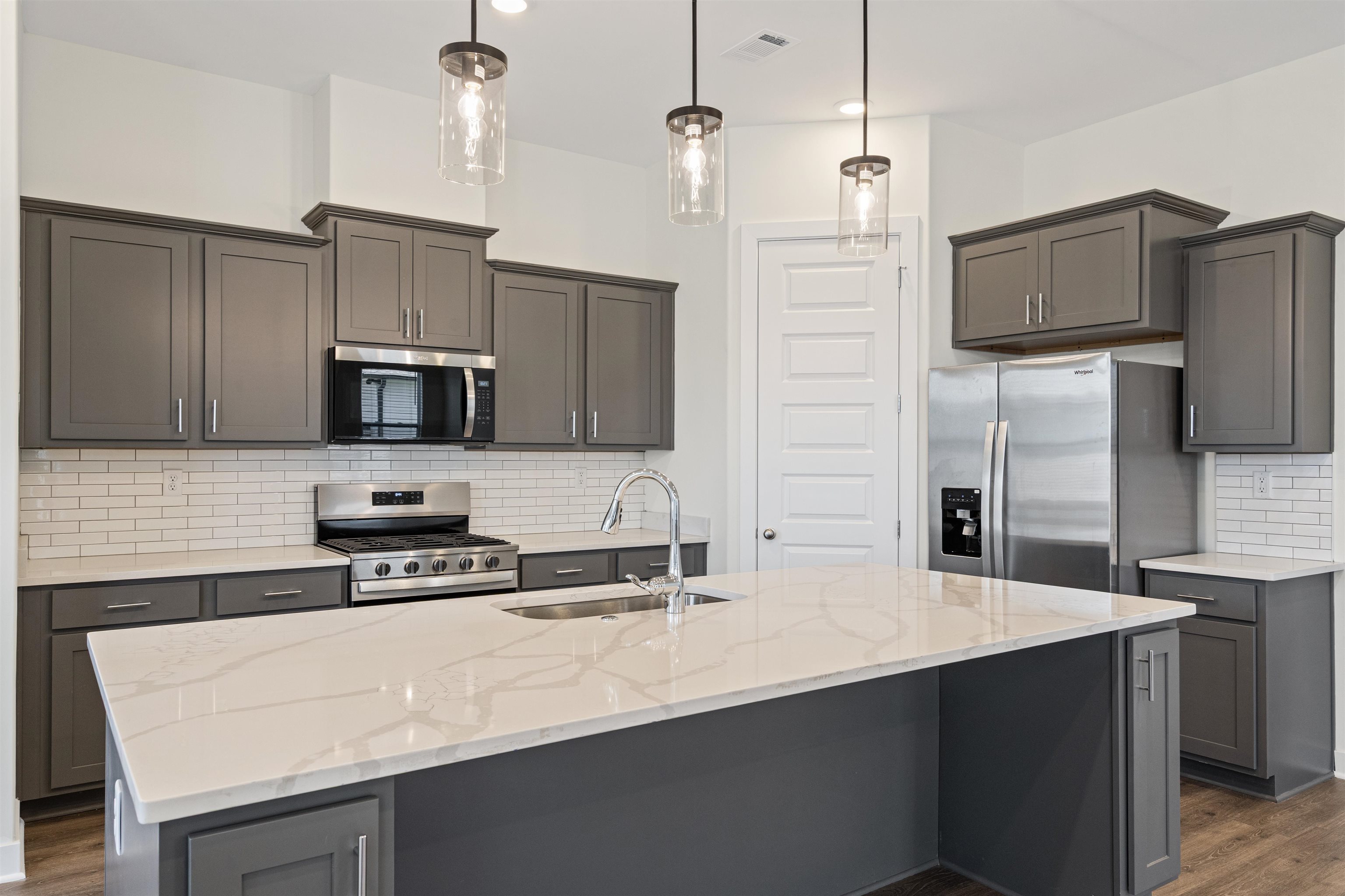 5666 Pleasant Pk Place Arlington, TN 38002 - Photo 14 of 27 Contemporary kitchen featuring a large island with a quartz countertop, gray shaker-style cabinetry, stainless steel appliances, and a white subway tile backsplash