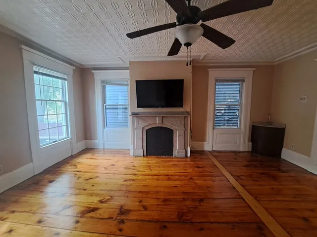 a view of a livingroom with a fireplace a ceiling fan and windows