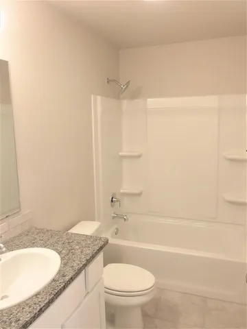 a bathroom with a granite countertop bathtub sink vanity mirror and toilet