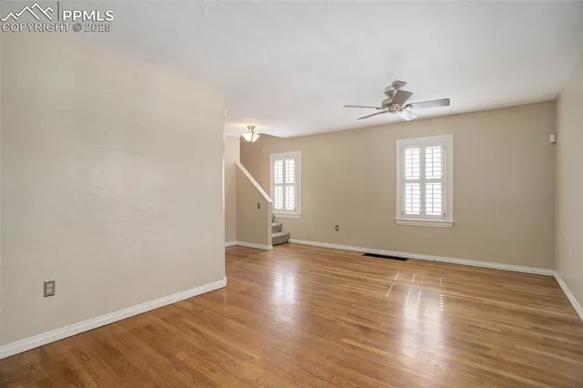 an empty room with wooden floor chandelier fan and windows