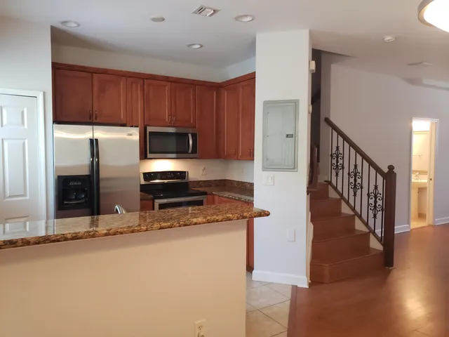 a kitchen with stainless steel appliances granite countertop a refrigerator a stove top oven and a sink with wooden floor