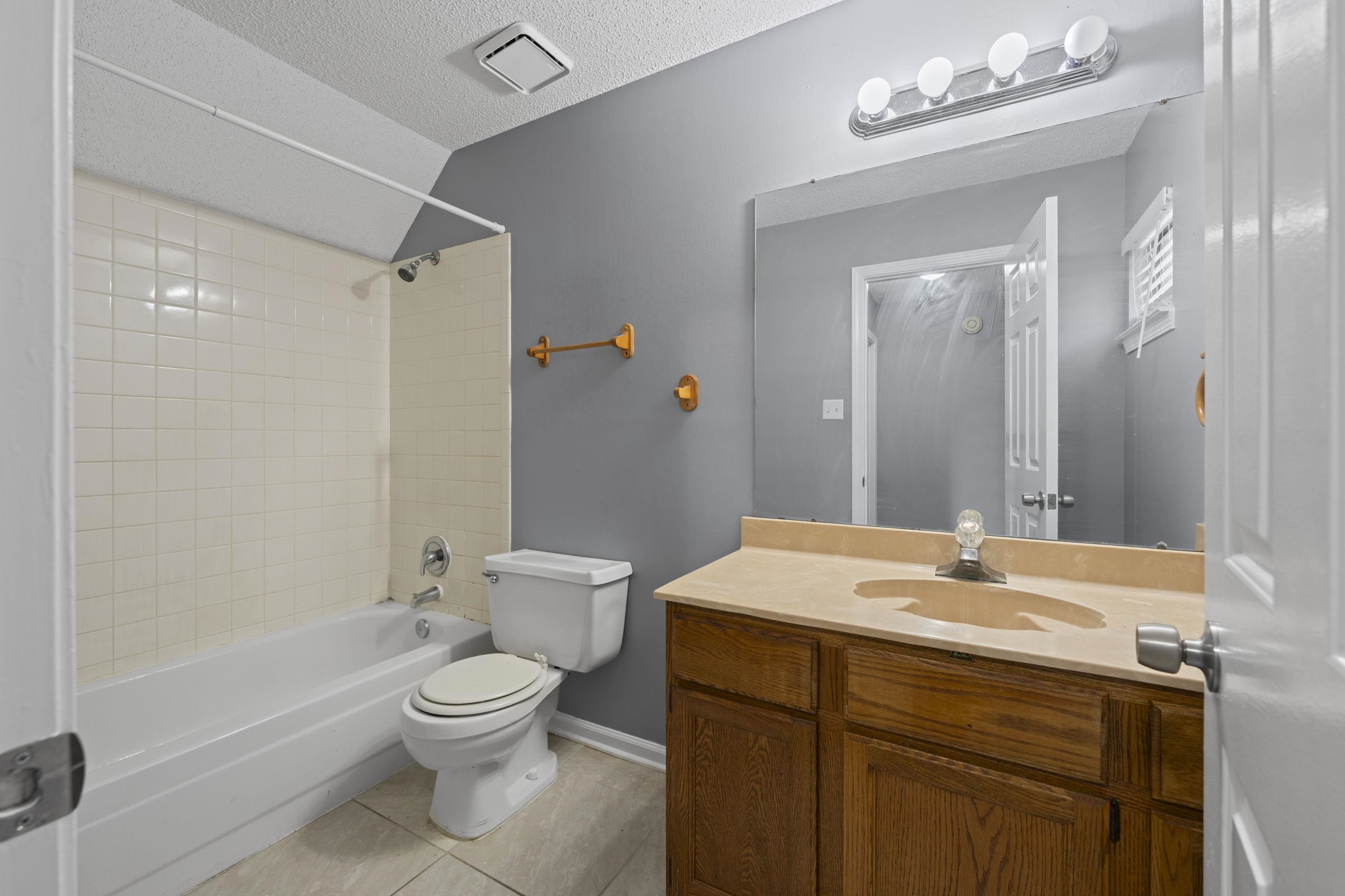 2252 Mangum Road Memphis, TN 38134 - Photo 17 of 23 Bathroom featuring a built-in tub with tile surround, a toilet, a wood-finish vanity with an integrated sink, a large wall mirror, and overhead lighting