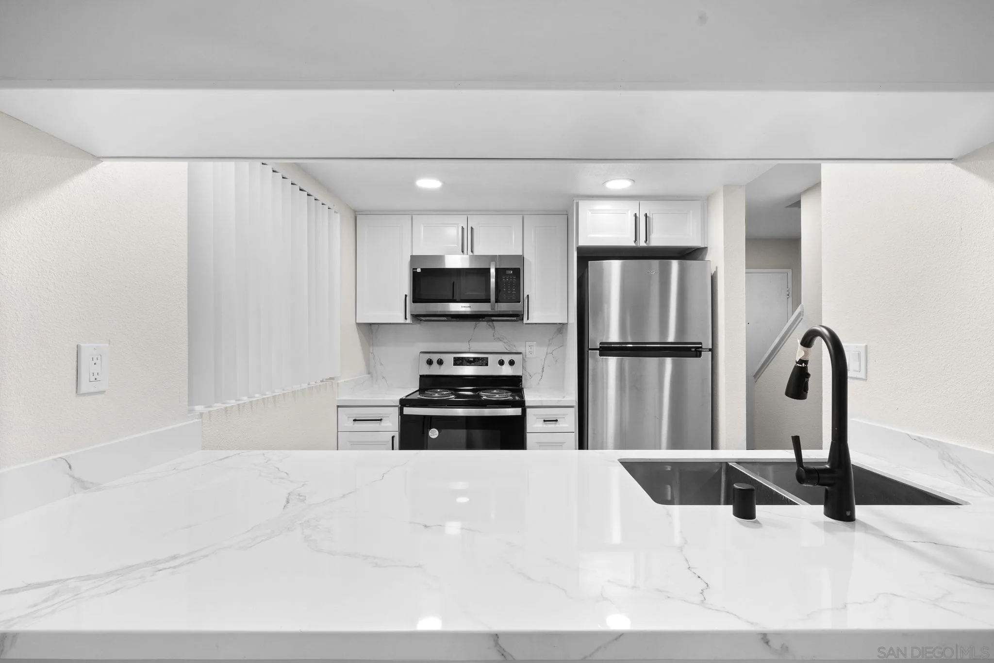 a kitchen with stainless steel appliances kitchen island granite countertop a refrigerator a stove a sink and white cabinets with wooden floor