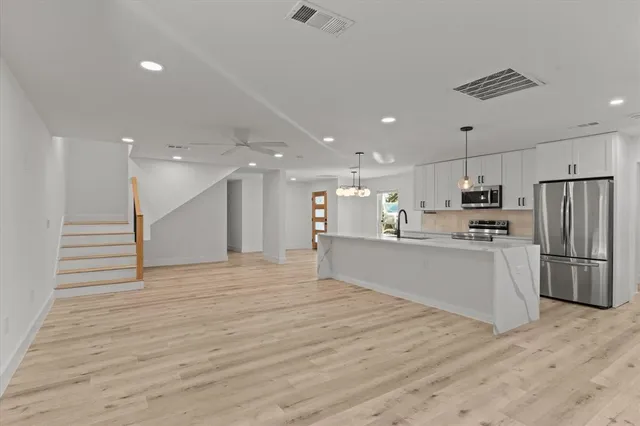 a large white kitchen with kitchen island a sink stainless steel appliances and cabinets